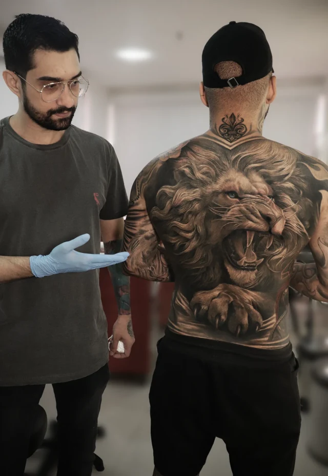 Lucas Franca ao lado de um cliente com uma tatuagem realista de leão nas costas